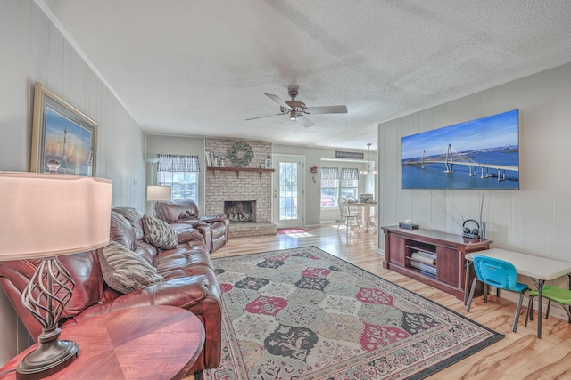 living area featuring a textured ceiling, ceiling fan, a fireplace, and wood finished floors