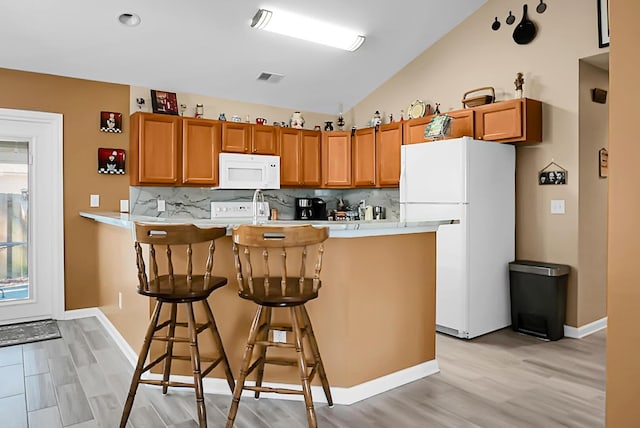 kitchen featuring a breakfast bar, white appliances, decorative backsplash, light hardwood / wood-style floors, and kitchen peninsula