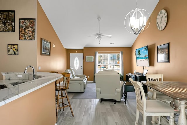 living room featuring ceiling fan with notable chandelier, vaulted ceiling, sink, and light hardwood / wood-style flooring