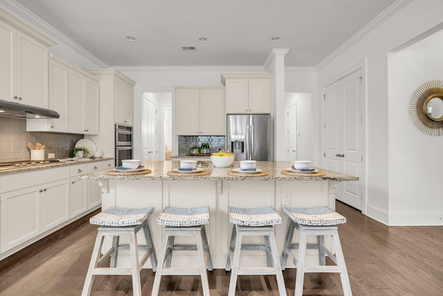 kitchen with stainless steel appliances, white cabinets, light stone counters, a kitchen island, and crown molding