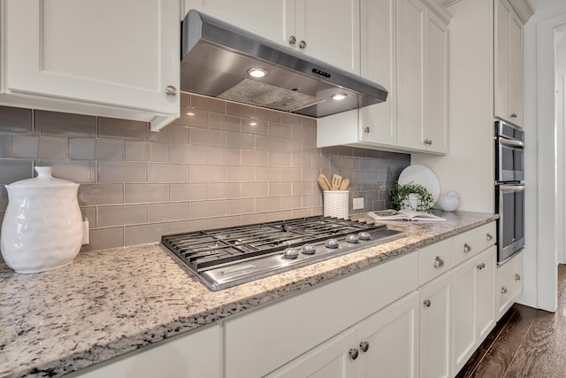 kitchen with stainless steel appliances, white cabinets, decorative backsplash, light stone countertops, and range hood