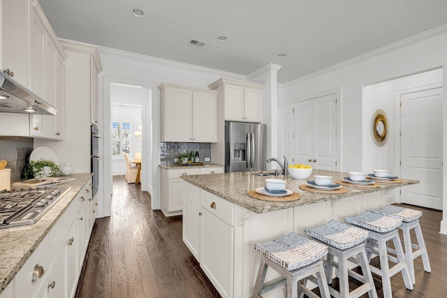 kitchen with light stone countertops, stainless steel appliances, white cabinetry, and a center island with sink