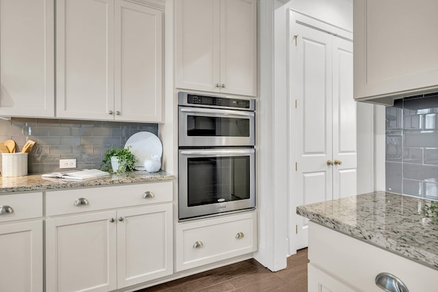 kitchen with stainless steel double oven, light stone countertops, decorative backsplash, and white cabinetry