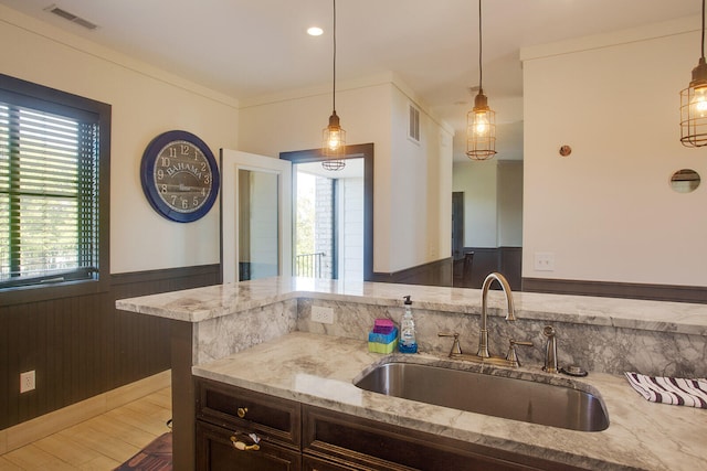 kitchen featuring decorative light fixtures, light stone counters, dark brown cabinetry, and sink