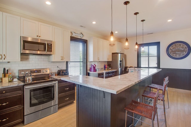 kitchen featuring appliances with stainless steel finishes, white cabinets, a center island with sink, light stone counters, and tasteful backsplash