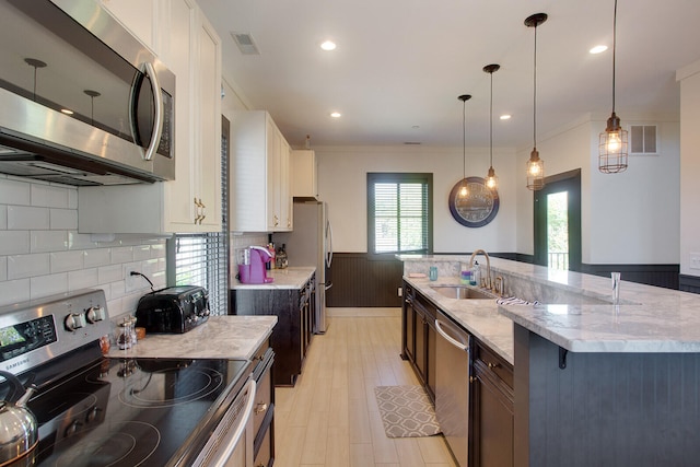 kitchen with sink, light stone counters, white cabinets, stainless steel appliances, and decorative light fixtures