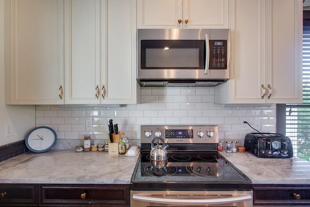 kitchen featuring tasteful backsplash, stainless steel appliances, white cabinetry, and light stone countertops