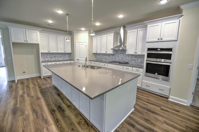 kitchen with appliances with stainless steel finishes, decorative light fixtures, white cabinetry, sink, and wall chimney range hood