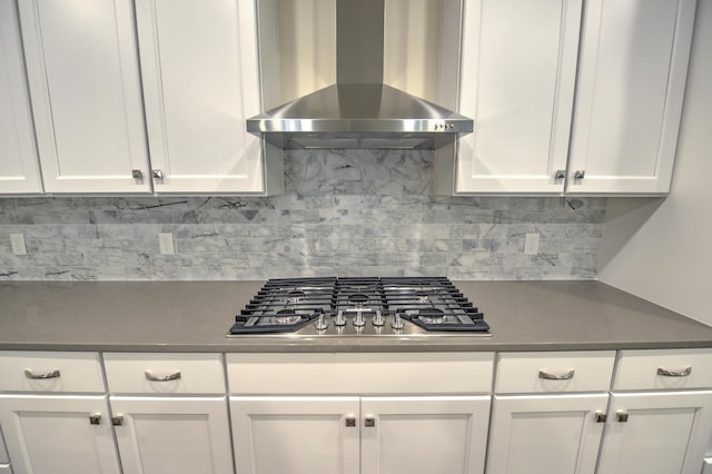 kitchen featuring wall chimney range hood, decorative backsplash, stainless steel gas cooktop, and white cabinets