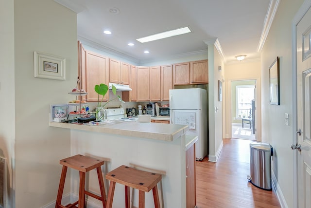 kitchen featuring crown molding, white appliances, a kitchen breakfast bar, kitchen peninsula, and light brown cabinets