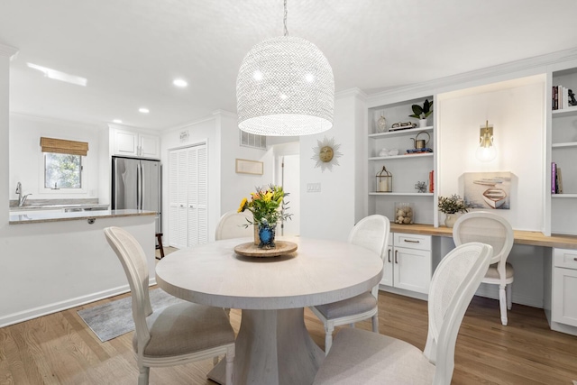 dining area featuring ornamental molding, built in desk, and light wood-type flooring