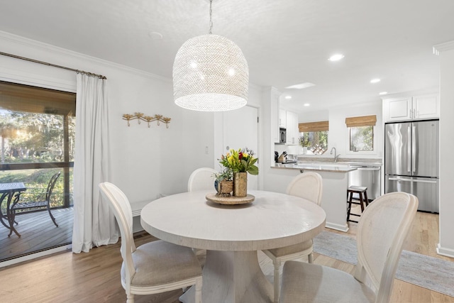 dining area featuring sink, ornamental molding, and light wood-type flooring