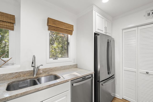 kitchen with appliances with stainless steel finishes, sink, white cabinets, light stone counters, and crown molding