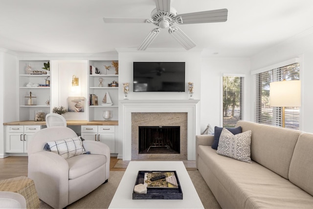 living room featuring crown molding, built in desk, light wood-type flooring, and built in shelves