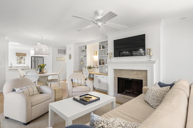 living room featuring ceiling fan, ornamental molding, sink, and built in features