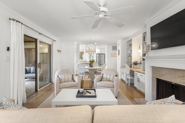 living room with crown molding, built in features, ceiling fan, and light wood-type flooring