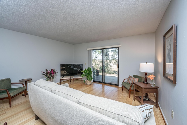 living room with baseboards, light wood-style flooring, and a textured ceiling