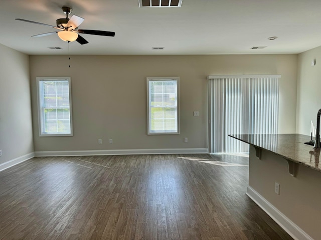 unfurnished living room with ceiling fan, a wealth of natural light, and dark wood-type flooring