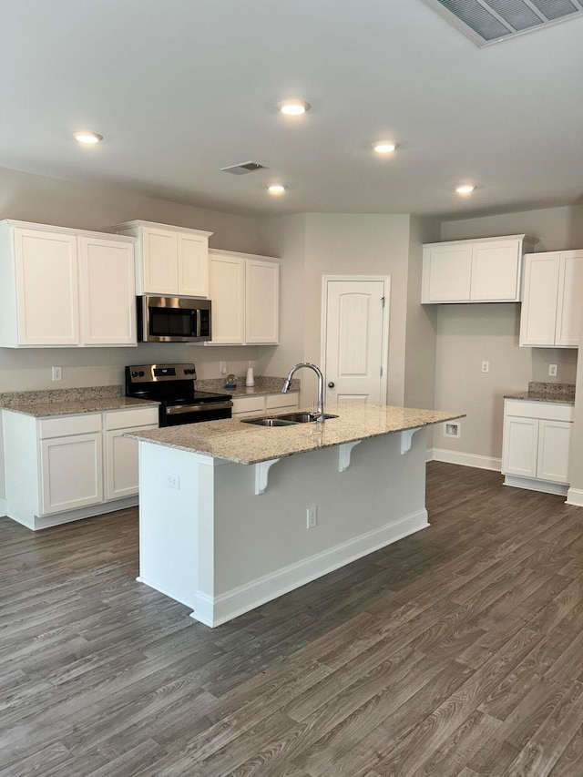 kitchen with dark hardwood / wood-style floors, sink, white cabinetry, appliances with stainless steel finishes, and a center island with sink