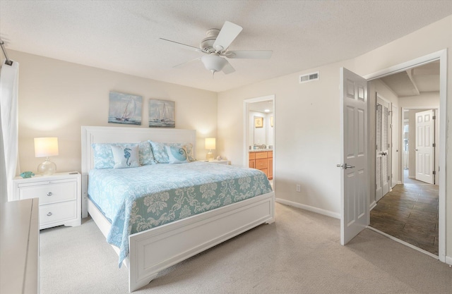 bedroom with ceiling fan, light carpet, connected bathroom, and a textured ceiling