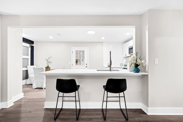 kitchen featuring white cabinets, sink, kitchen peninsula, hardwood / wood-style flooring, and a kitchen breakfast bar