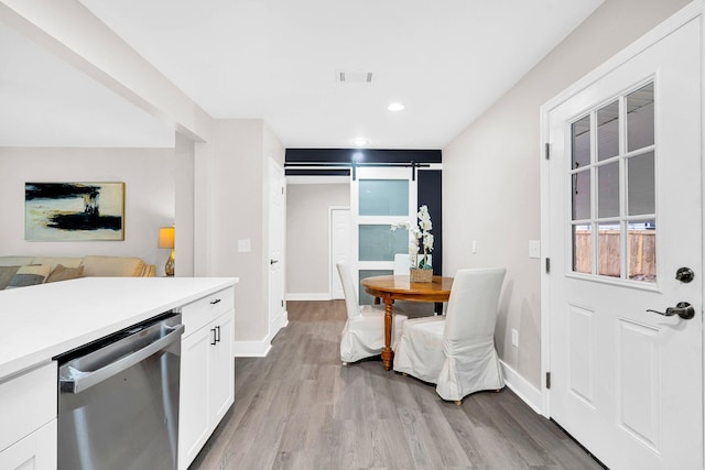 kitchen featuring white cabinets, dishwasher, a barn door, and light hardwood / wood-style floors