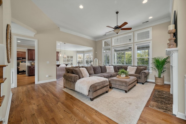 living area with baseboards, light wood-style floors, visible vents, and crown molding