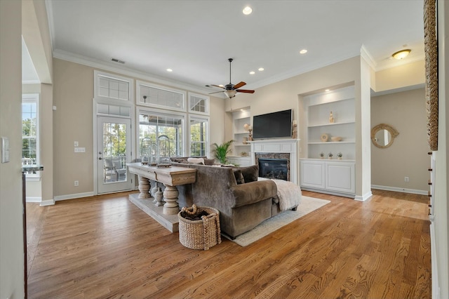 living area featuring light wood-style flooring, ornamental molding, a wealth of natural light, and a glass covered fireplace