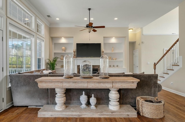 living area featuring built in features, dark wood-style flooring, a fireplace, and ornamental molding