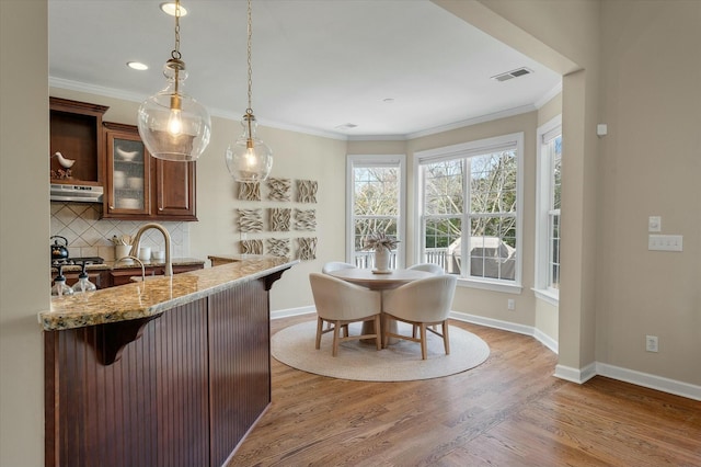 kitchen with light wood-style flooring, under cabinet range hood, a breakfast bar, decorative backsplash, and crown molding