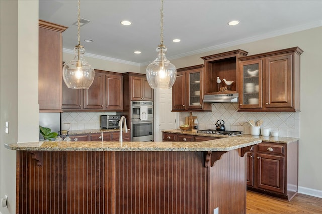 kitchen with appliances with stainless steel finishes, under cabinet range hood, a kitchen bar, and light stone countertops