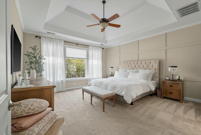 bedroom featuring light carpet, visible vents, a raised ceiling, and a decorative wall