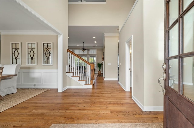 foyer with ornamental molding, stairs, light wood-style floors, a decorative wall, and recessed lighting