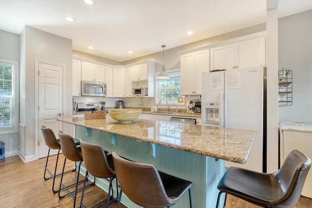 kitchen featuring stainless steel appliances, decorative light fixtures, a breakfast bar area, and white cabinets