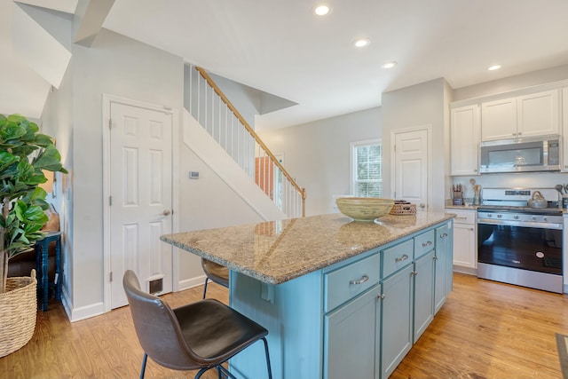 kitchen with light stone counters, a kitchen island, white cabinets, and appliances with stainless steel finishes