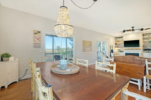 dining area featuring ceiling fan with notable chandelier, hardwood / wood-style floors, and built in features