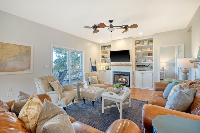 living room featuring a fireplace, wood-type flooring, built in features, and ceiling fan