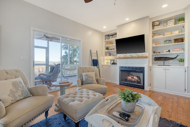 living room with hardwood / wood-style flooring, built in features, and ceiling fan