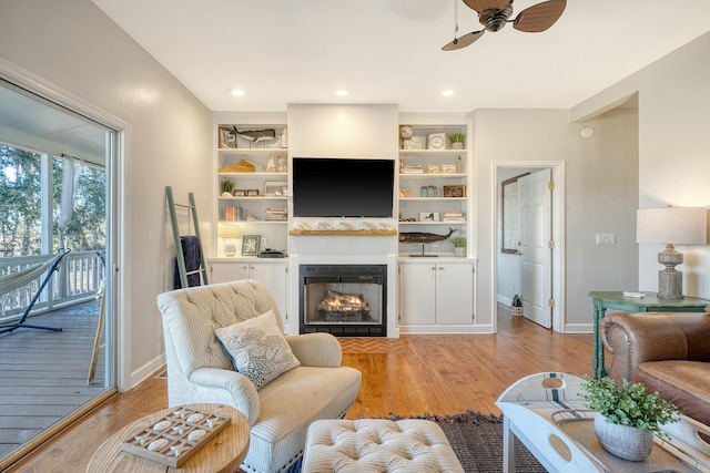 living room featuring built in features, ceiling fan, and light wood-type flooring