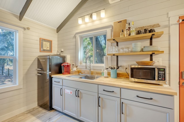 kitchen featuring sink, wooden counters, appliances with stainless steel finishes, vaulted ceiling with beams, and wood walls