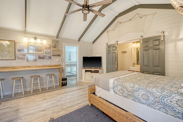 bedroom featuring high vaulted ceiling, beam ceiling, a barn door, ensuite bath, and light hardwood / wood-style flooring