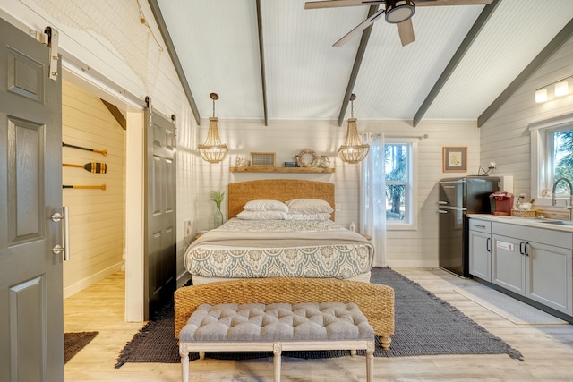 bedroom featuring lofted ceiling with beams, a barn door, black refrigerator, and light hardwood / wood-style flooring