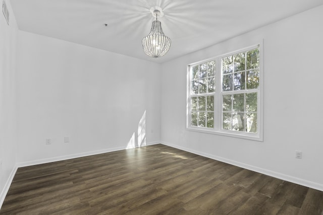 spare room with a chandelier, dark wood-style flooring, and baseboards