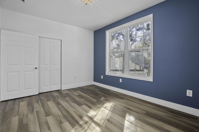 unfurnished bedroom featuring dark wood-style flooring, a closet, and baseboards