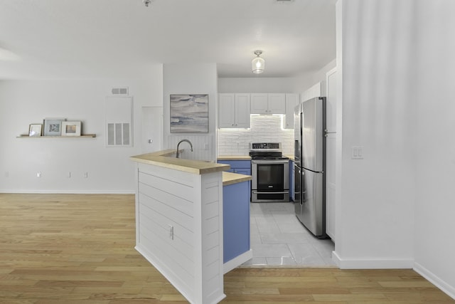 kitchen featuring a sink, white cabinetry, appliances with stainless steel finishes, light wood-type flooring, and tasteful backsplash