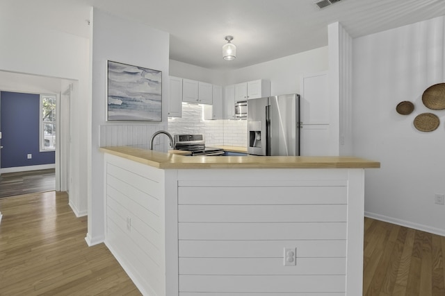 kitchen with decorative backsplash, appliances with stainless steel finishes, a peninsula, light countertops, and white cabinetry