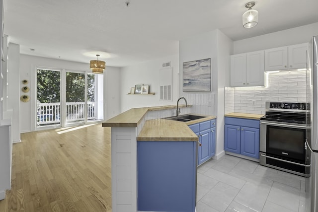 kitchen featuring stainless steel electric range oven, butcher block counters, blue cabinetry, white cabinetry, and a sink