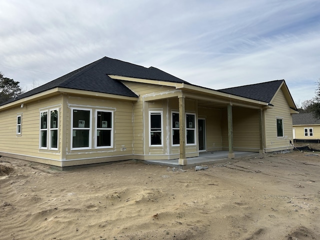 back of property with a shingled roof and a patio