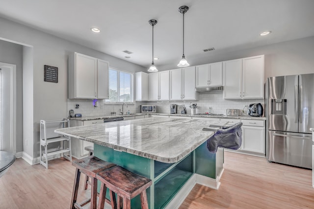 kitchen with a kitchen breakfast bar, hanging light fixtures, white cabinets, a kitchen island, and stainless steel appliances