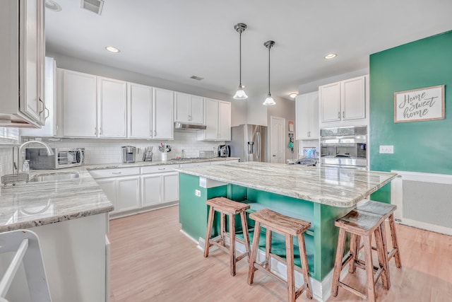 kitchen featuring white cabinetry, a kitchen island, a breakfast bar area, stainless steel appliances, and decorative light fixtures